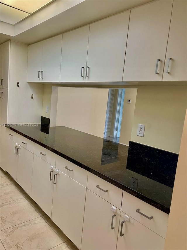 kitchen with white cabinetry, dark stone counters, and light tile patterned floors