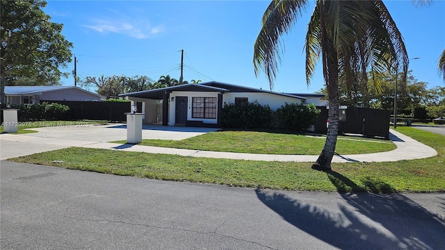 view of front of property with driveway, an attached carport, fence, a front lawn, and stucco siding