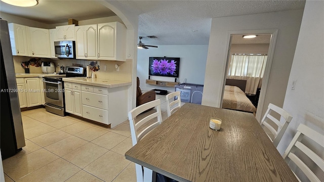 kitchen featuring tile countertops, ceiling fan, a textured ceiling, light tile patterned floors, and appliances with stainless steel finishes