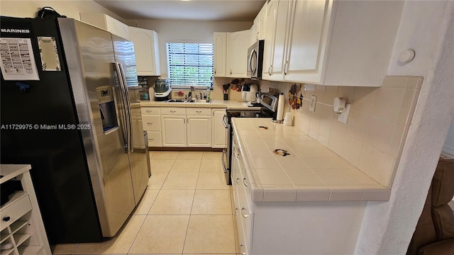 kitchen featuring tile countertops, appliances with stainless steel finishes, light tile patterned floors, and white cabinets