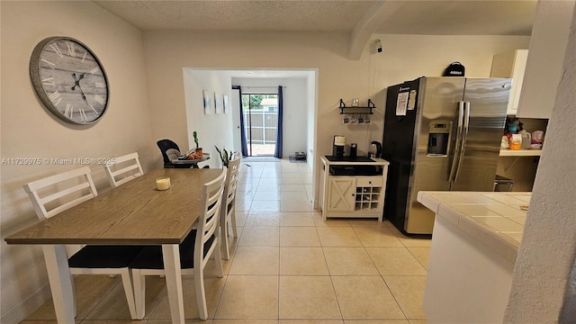 kitchen featuring light tile patterned floors, stainless steel refrigerator with ice dispenser, a textured ceiling, and tile countertops