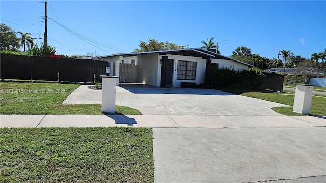 mid-century home featuring driveway, stucco siding, fence, and a front yard