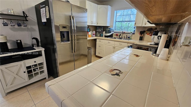 kitchen with tile countertops, white cabinets, stainless steel refrigerator with ice dispenser, and a sink