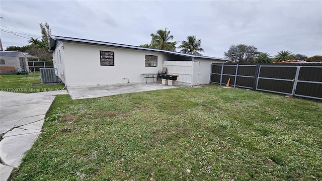 rear view of property featuring a lawn, fence, a patio area, central AC, and stucco siding