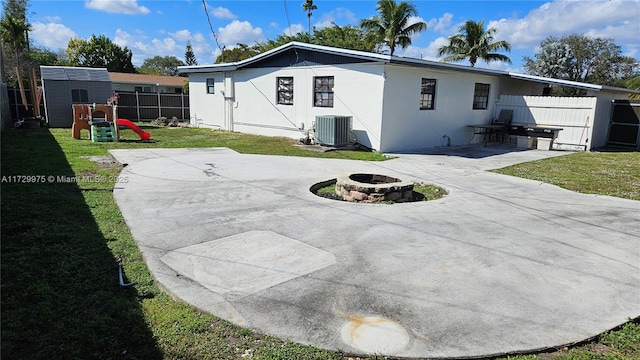 rear view of property featuring a playground, a yard, a patio, central AC, and fence