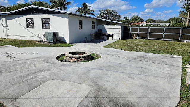 view of side of property featuring a fire pit, fence, cooling unit, a yard, and stucco siding