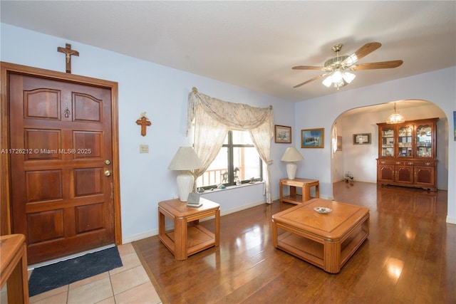 living area featuring a ceiling fan, arched walkways, light wood finished floors, and baseboards