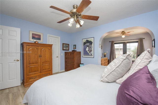 bedroom featuring arched walkways, a ceiling fan, light wood-style floors, and access to outside