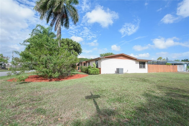 view of side of property featuring stucco siding, a lawn, central AC, and fence