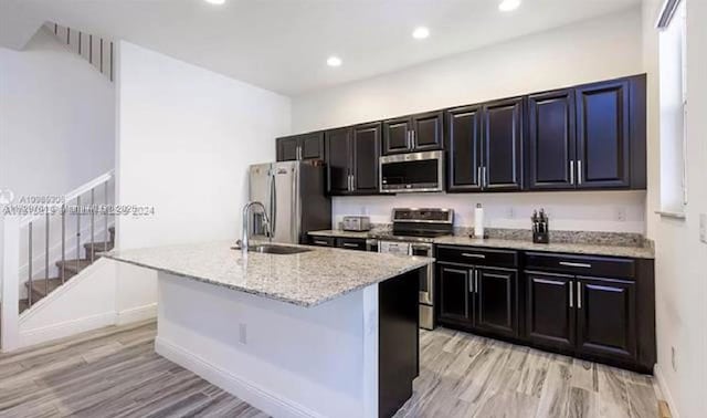 kitchen with sink, a center island with sink, light stone counters, and appliances with stainless steel finishes