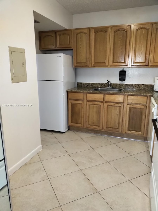 kitchen featuring electric panel, white fridge, dark stone countertops, sink, and light tile patterned floors