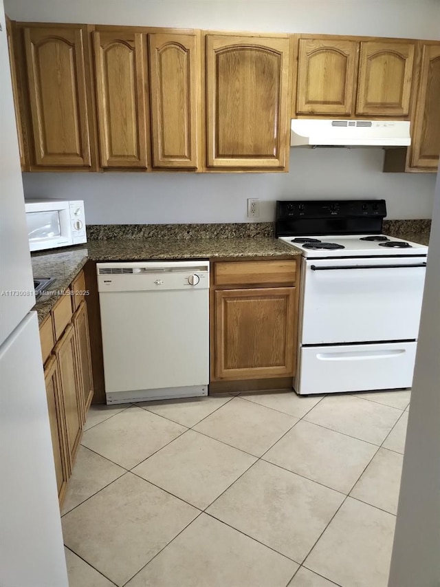 kitchen with dark stone counters, white appliances, and light tile patterned flooring