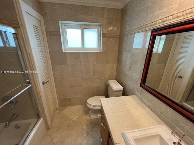 full bathroom featuring tile walls, toilet, vanity, ornamental molding, and bath / shower combo with glass door