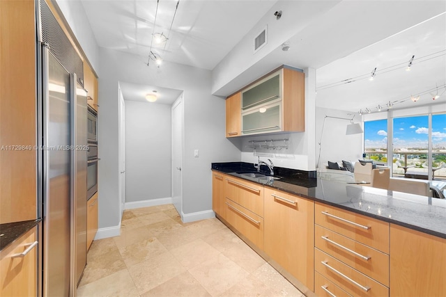 kitchen featuring sink, dark stone countertops, appliances with stainless steel finishes, and light brown cabinets