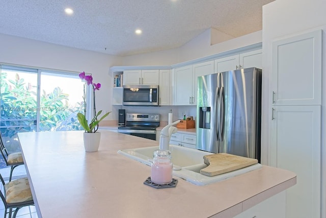 kitchen with a breakfast bar, appliances with stainless steel finishes, white cabinetry, a kitchen island with sink, and a textured ceiling