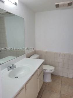 bathroom featuring vanity, toilet, tile patterned floors, and tile walls