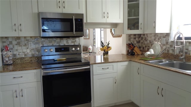 kitchen featuring appliances with stainless steel finishes, sink, white cabinets, dark stone countertops, and decorative backsplash