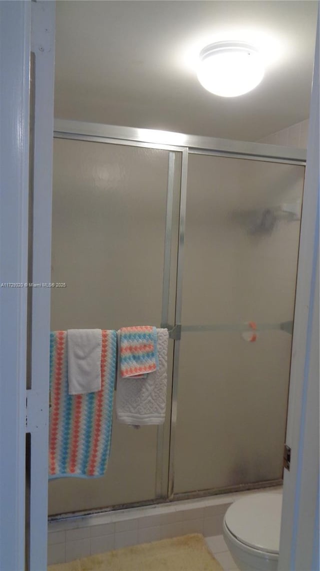 bathroom with a shower with door, toilet, and tile patterned floors