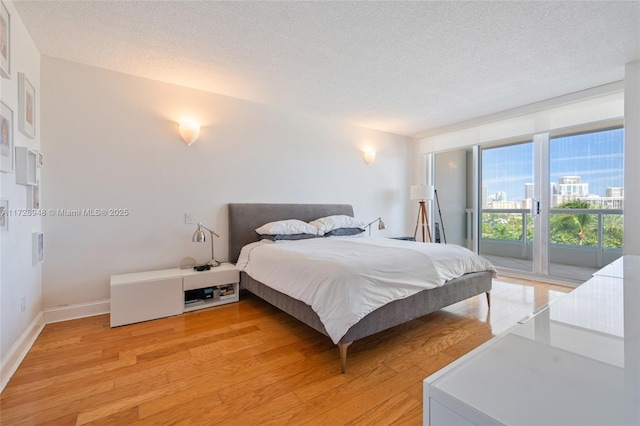 bedroom with baseboards, a city view, light wood-style flooring, and a textured ceiling