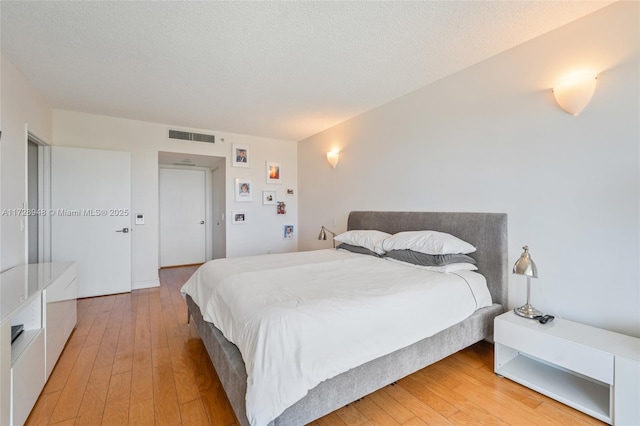 bedroom featuring light wood-type flooring, visible vents, and a textured ceiling