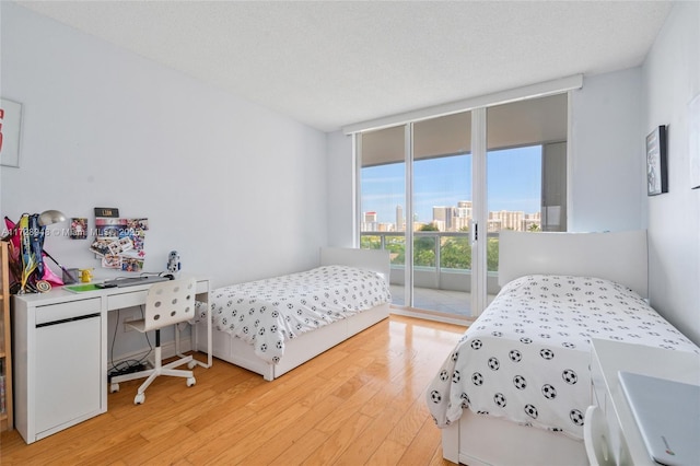 bedroom featuring access to exterior, a view of city, a textured ceiling, wood finished floors, and a wall of windows