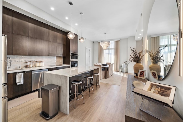 kitchen featuring light wood-type flooring, a kitchen island, dark brown cabinetry, decorative light fixtures, and stainless steel appliances