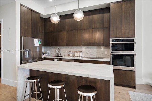 kitchen with pendant lighting, stainless steel appliances, decorative backsplash, sink, and light wood-type flooring