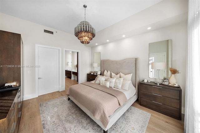 bedroom with light hardwood / wood-style floors, ensuite bathroom, and an inviting chandelier