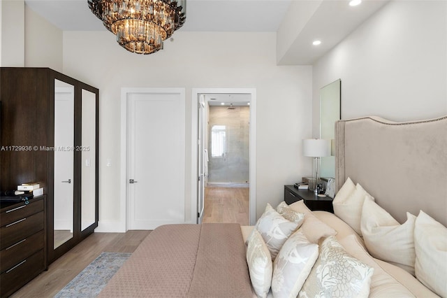 bedroom with a notable chandelier, ensuite bathroom, and light hardwood / wood-style flooring