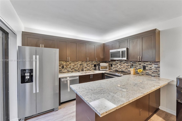 kitchen with stainless steel appliances, sink, kitchen peninsula, light wood-type flooring, and light stone counters