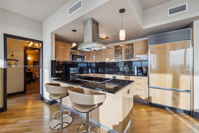 kitchen with a kitchen breakfast bar, hanging light fixtures, decorative backsplash, paneled built in refrigerator, and island range hood