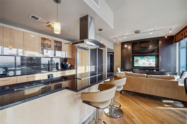 kitchen with pendant lighting, black electric stovetop, island range hood, light wood-type flooring, and a breakfast bar