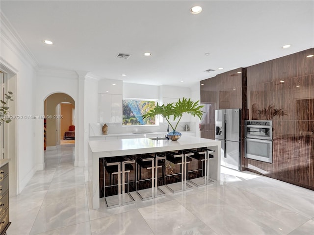 kitchen featuring a breakfast bar area, stainless steel appliances, a center island, dark brown cabinetry, and white cabinets