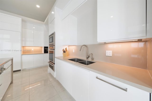 kitchen featuring appliances with stainless steel finishes, white cabinetry, sink, backsplash, and light tile patterned floors