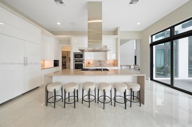 kitchen with white cabinets, a breakfast bar area, appliances with stainless steel finishes, and a large island with sink