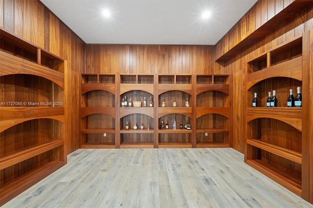 wine area with light hardwood / wood-style floors and wood walls