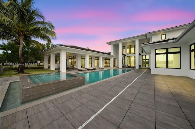 pool at dusk with an in ground hot tub and a patio