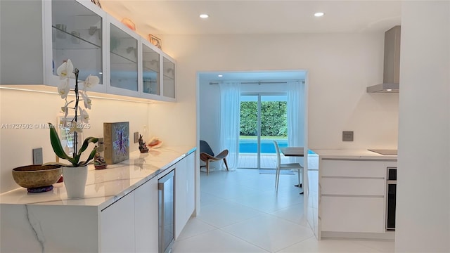 kitchen featuring wall chimney exhaust hood, black electric cooktop, white cabinets, and light stone counters