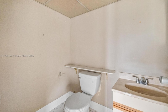 half bath with toilet, baseboards, a paneled ceiling, and vanity