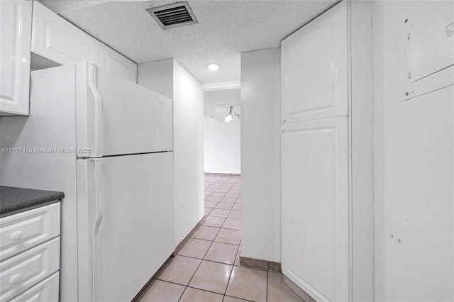 kitchen with white refrigerator, white cabinetry, light tile patterned floors, and a textured ceiling