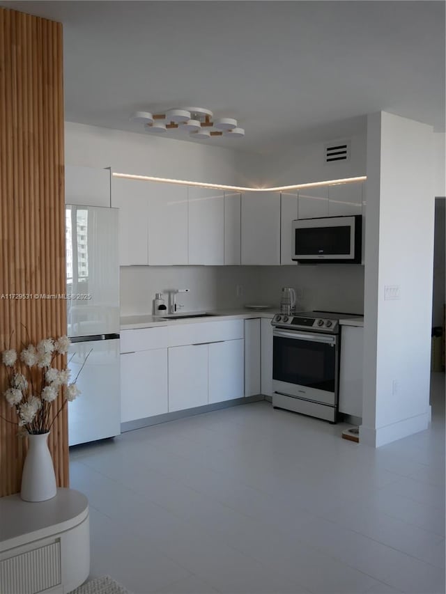 kitchen featuring sink, white fridge, white cabinetry, and stainless steel electric range