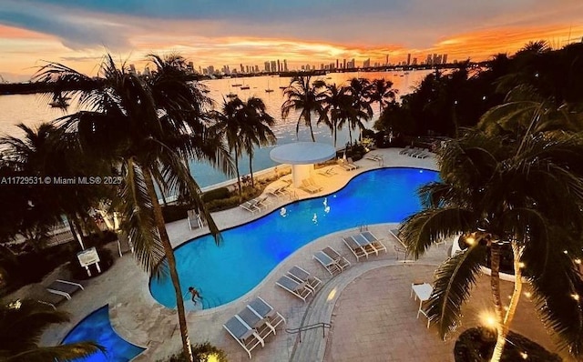 pool at dusk featuring a patio area and a water view