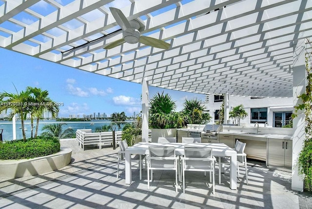 view of patio / terrace with grilling area, a pergola, a water view, and exterior kitchen