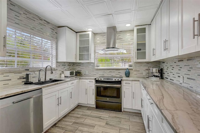 kitchen featuring sink, stainless steel appliances, white cabinetry, and wall chimney exhaust hood