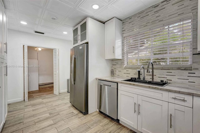 kitchen featuring appliances with stainless steel finishes, sink, backsplash, white cabinets, and light stone countertops