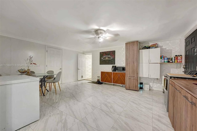 kitchen with crown molding, ceiling fan, appliances with stainless steel finishes, washer / dryer, and white cabinets