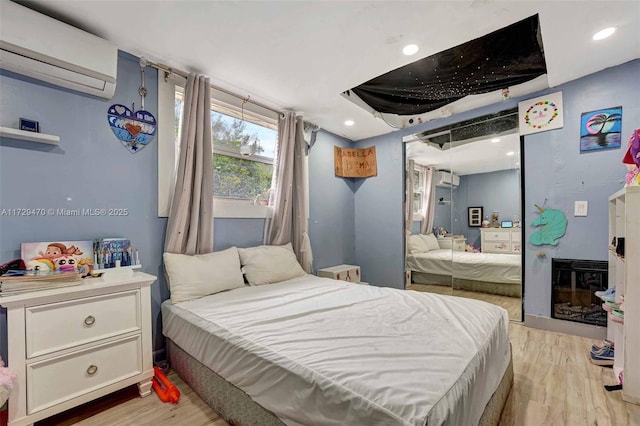 bedroom featuring an AC wall unit, a fireplace, and light wood-type flooring