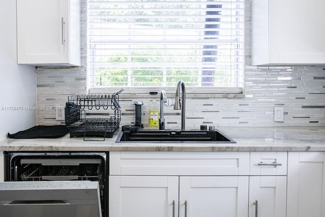 kitchen with light stone countertops, dishwashing machine, white cabinetry, sink, and backsplash