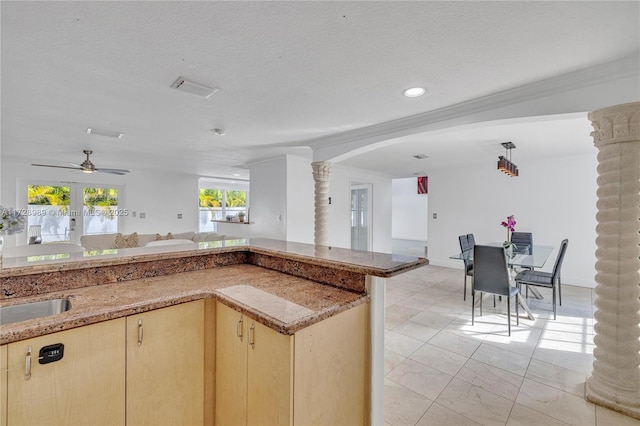 kitchen with a textured ceiling, ornate columns, light brown cabinetry, ceiling fan, and crown molding