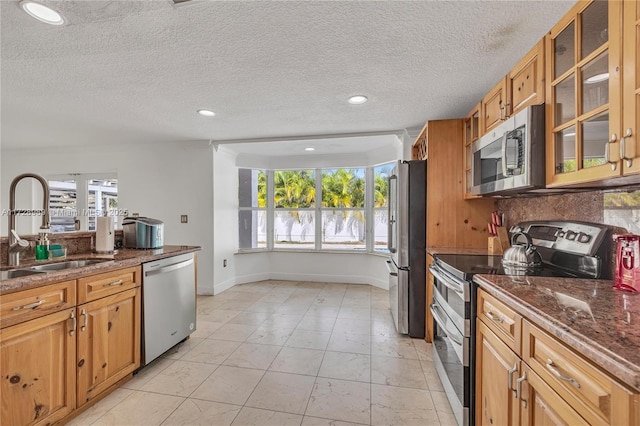 kitchen with sink, a textured ceiling, appliances with stainless steel finishes, and dark stone countertops